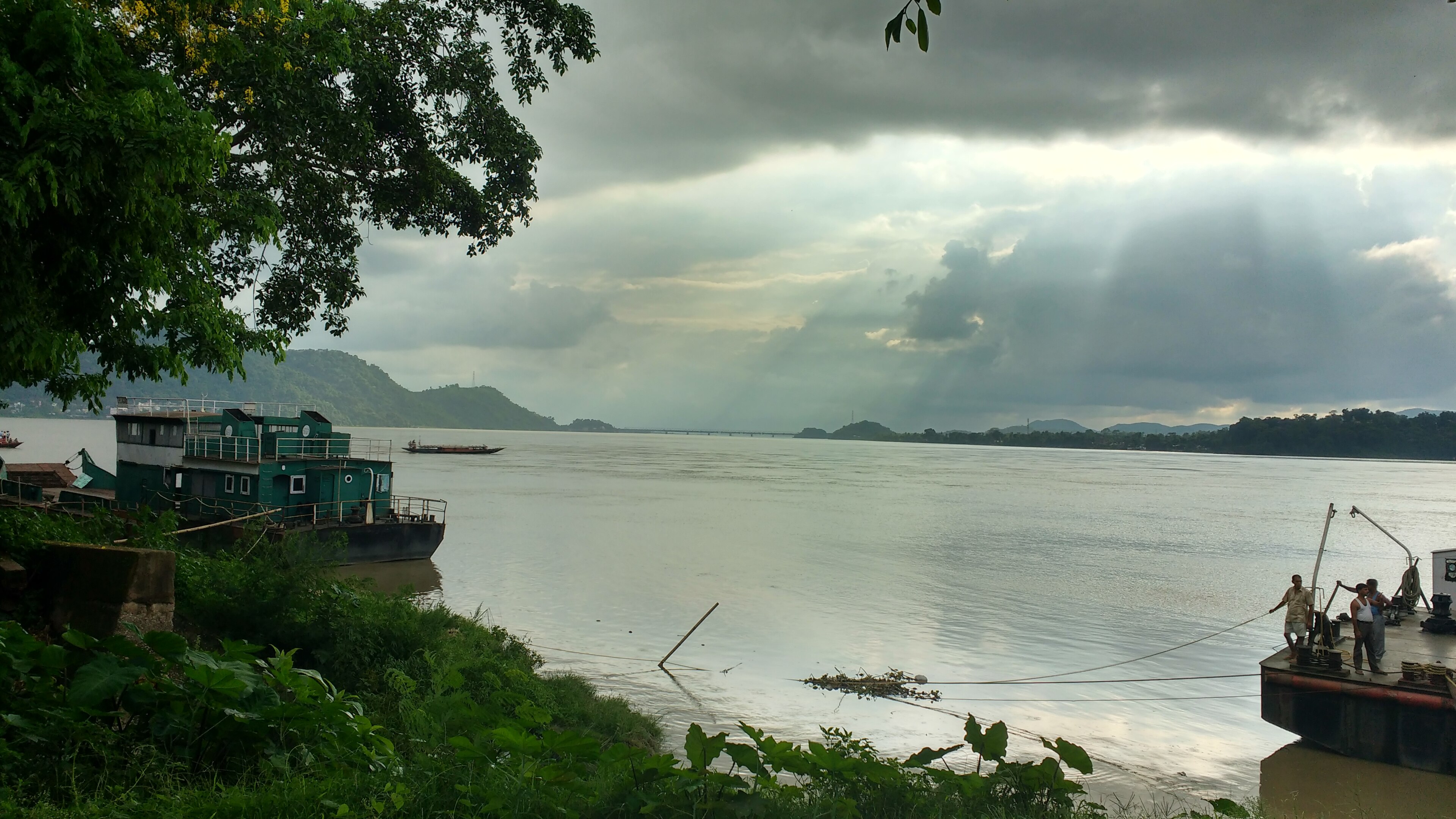 Working river craft and lush banks along the Brahmaputra channel in Assam